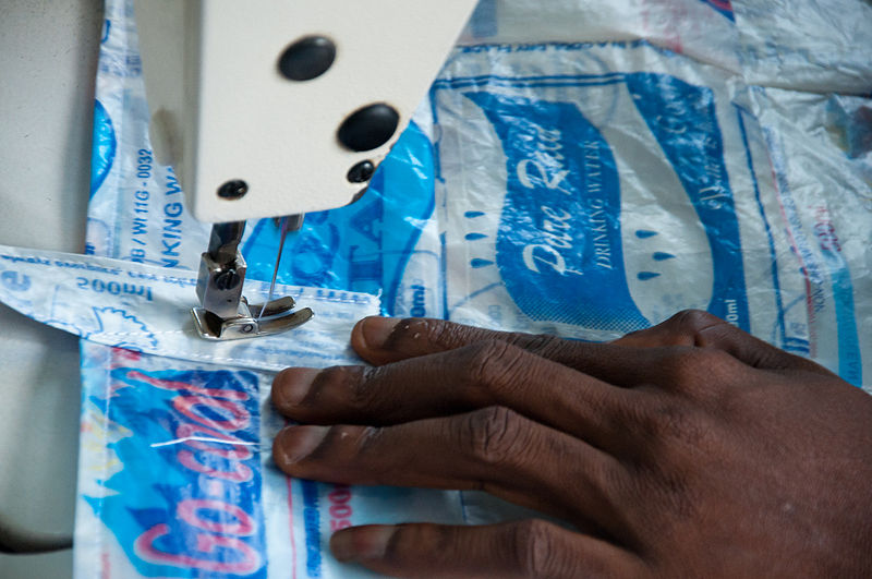 Woman sewing bags from discarded plastic material. By Tomas Prochazka. From Wikimedia Commons.